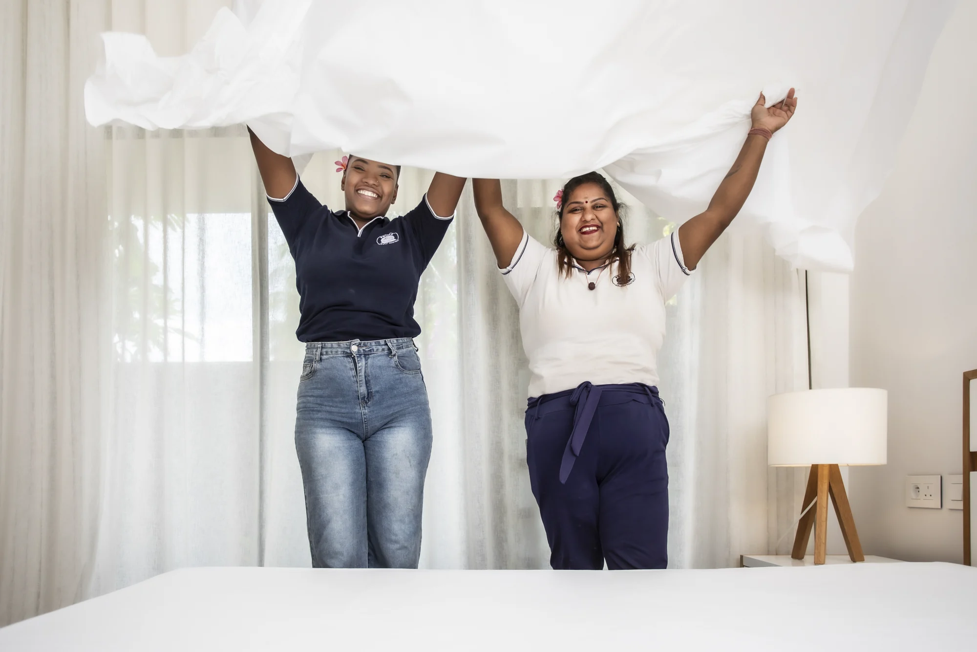 Deux membres de l’équipe Prima préparent un lit en déployant un drap blanc.